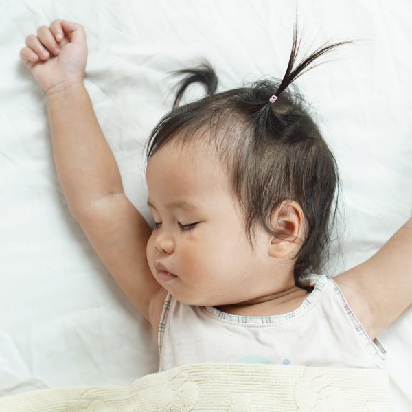 Cute toddler girl sleeping on white bed sheets cuddle in yellow blanket, bright room